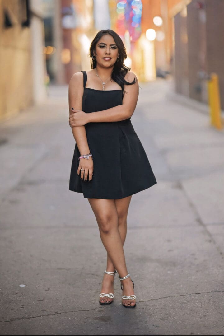 Woman in black dress standing in alley.
