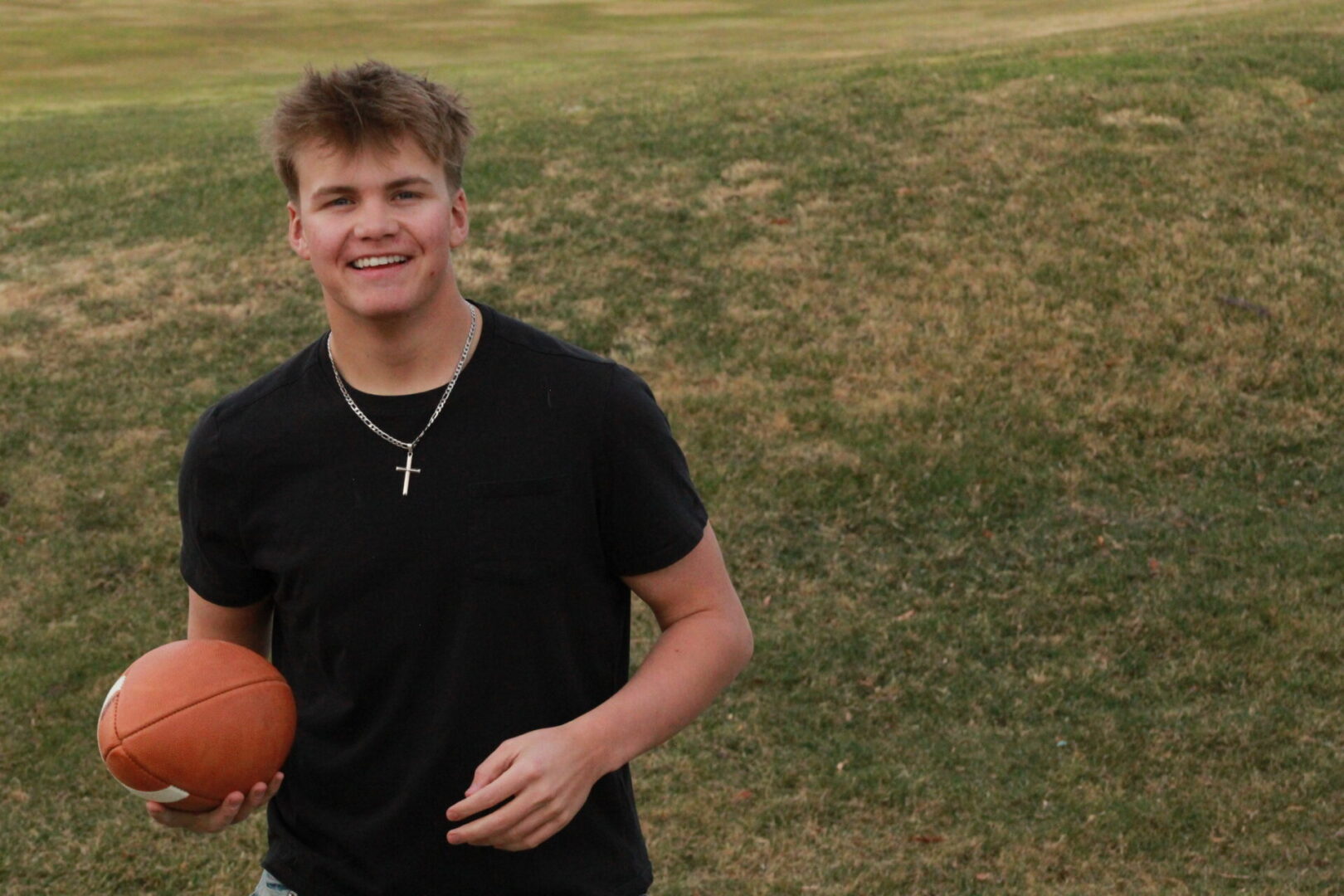 Smiling person holding football on grass.