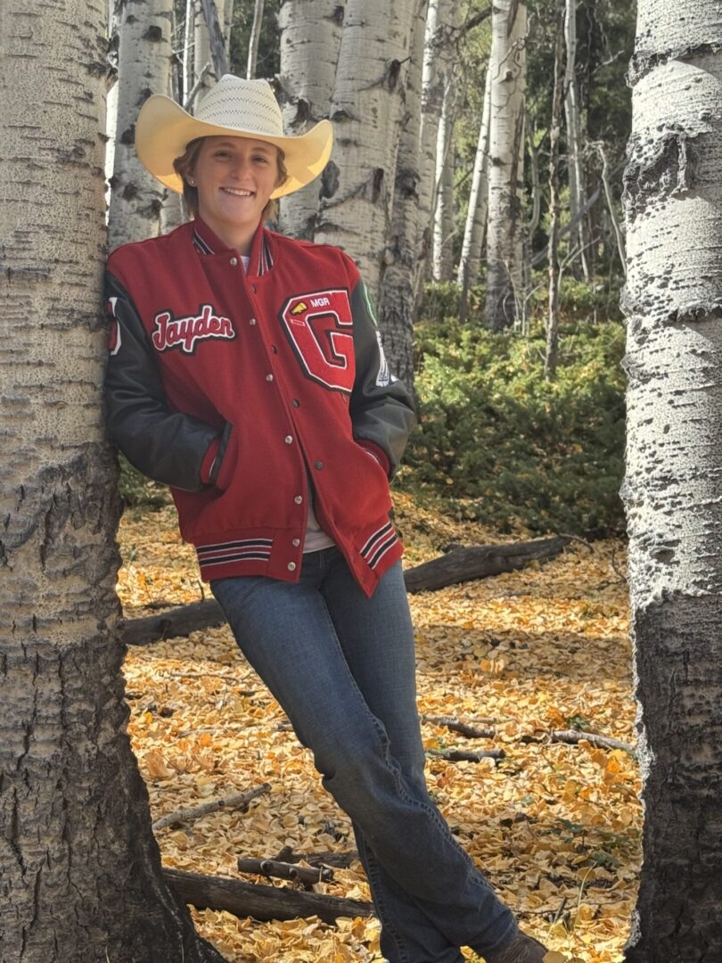 Person in cowboy hat leaning on tree.