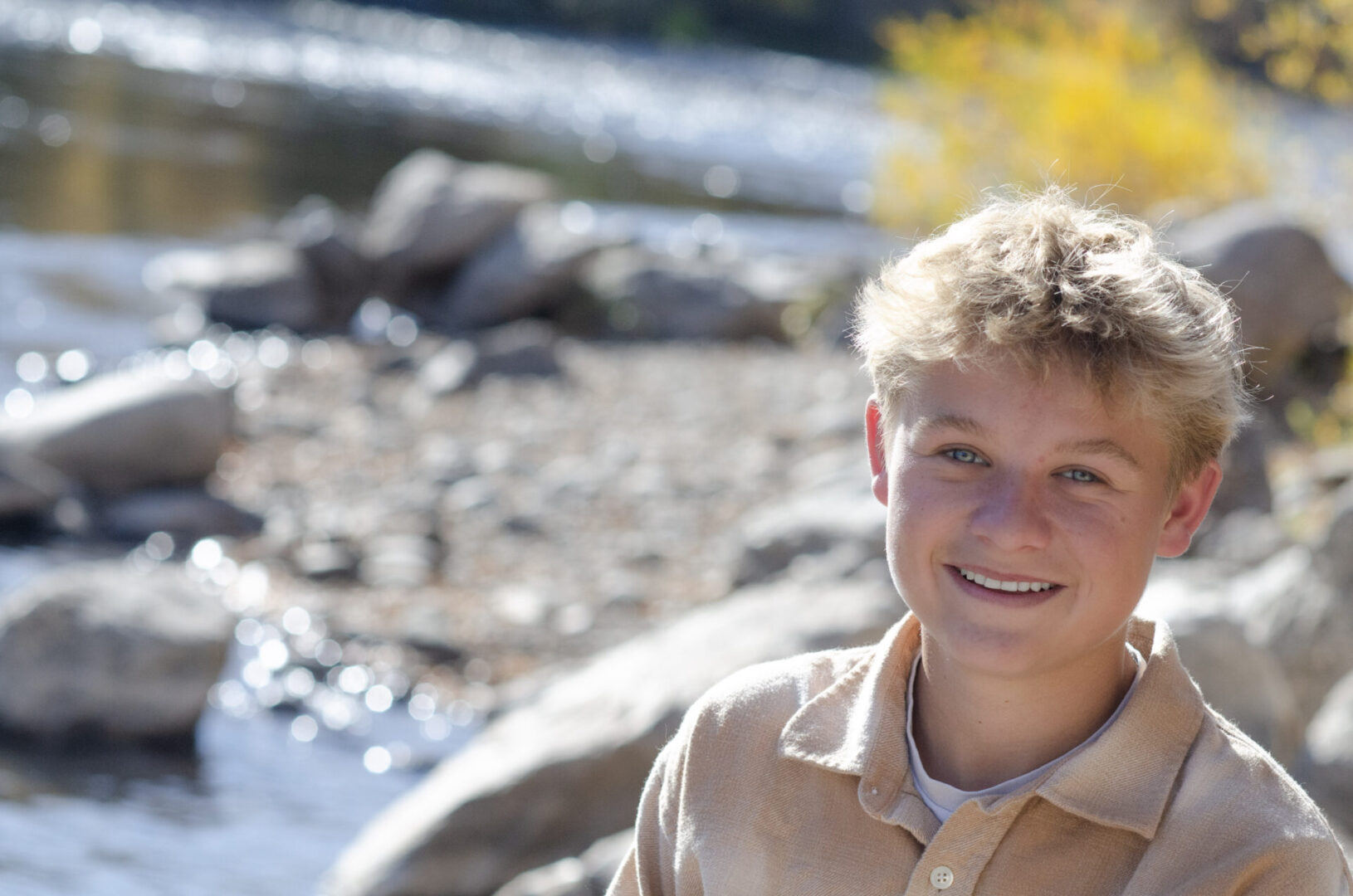 Smiling person beside a scenic riverbank.
