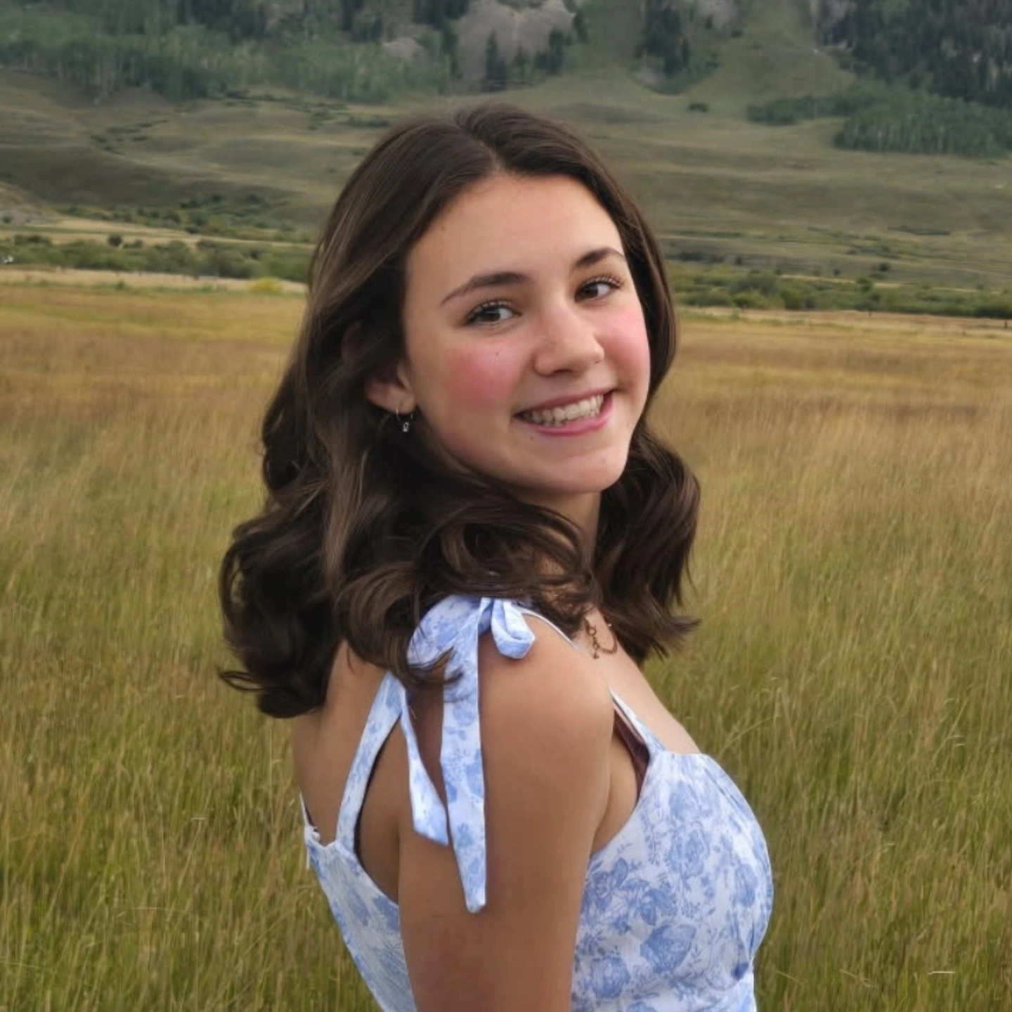Smiling girl in field wearing blue dress.