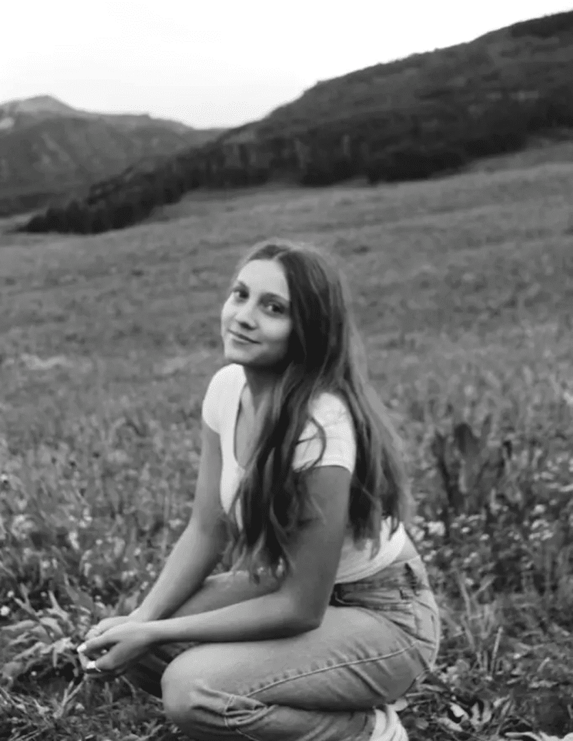 Woman in field with mountains behind her.