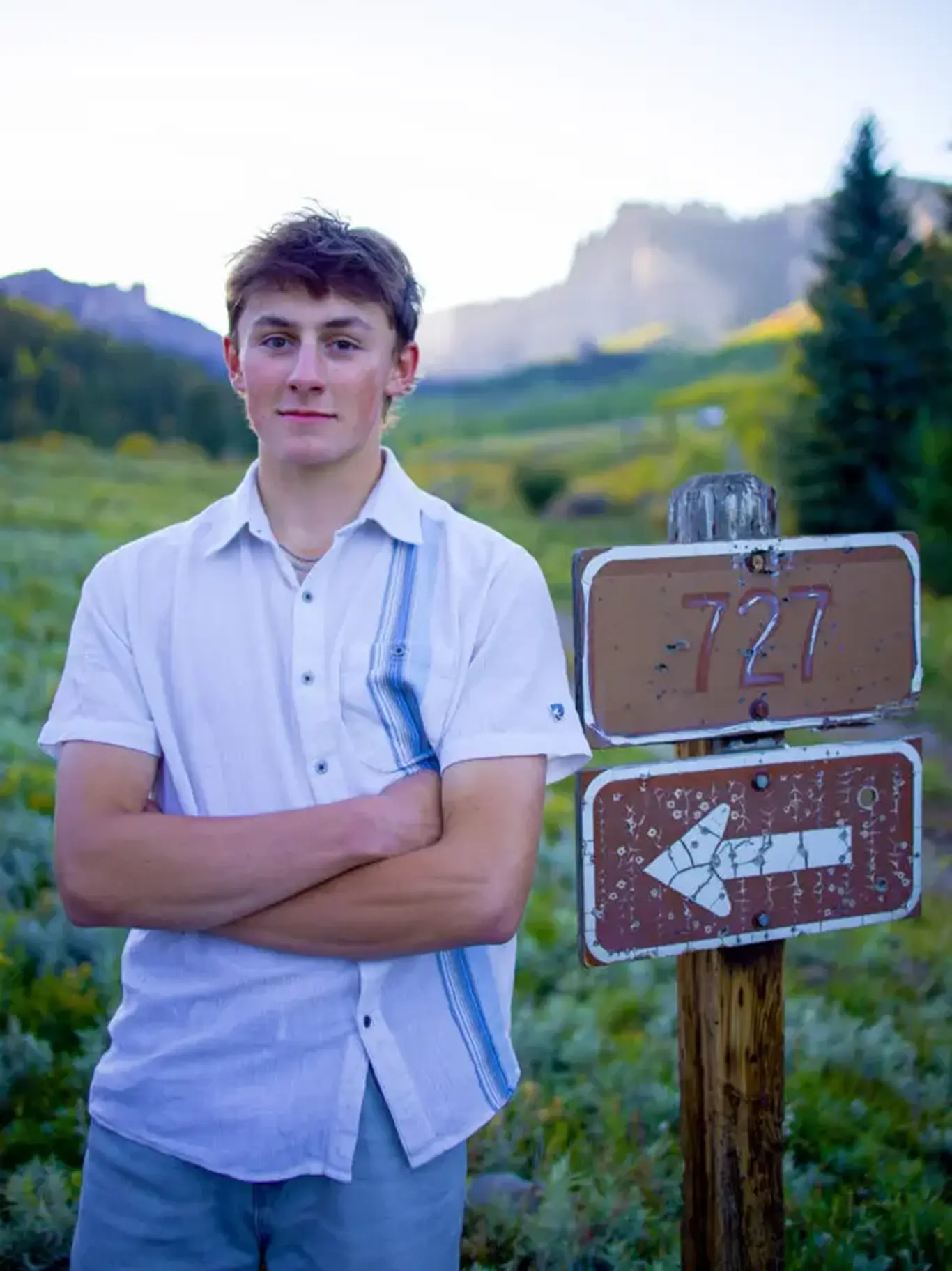 Young man standing beside trail sign outdoors.