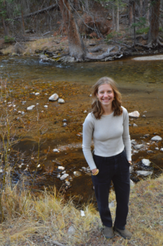 Smiling person standing beside forest stream