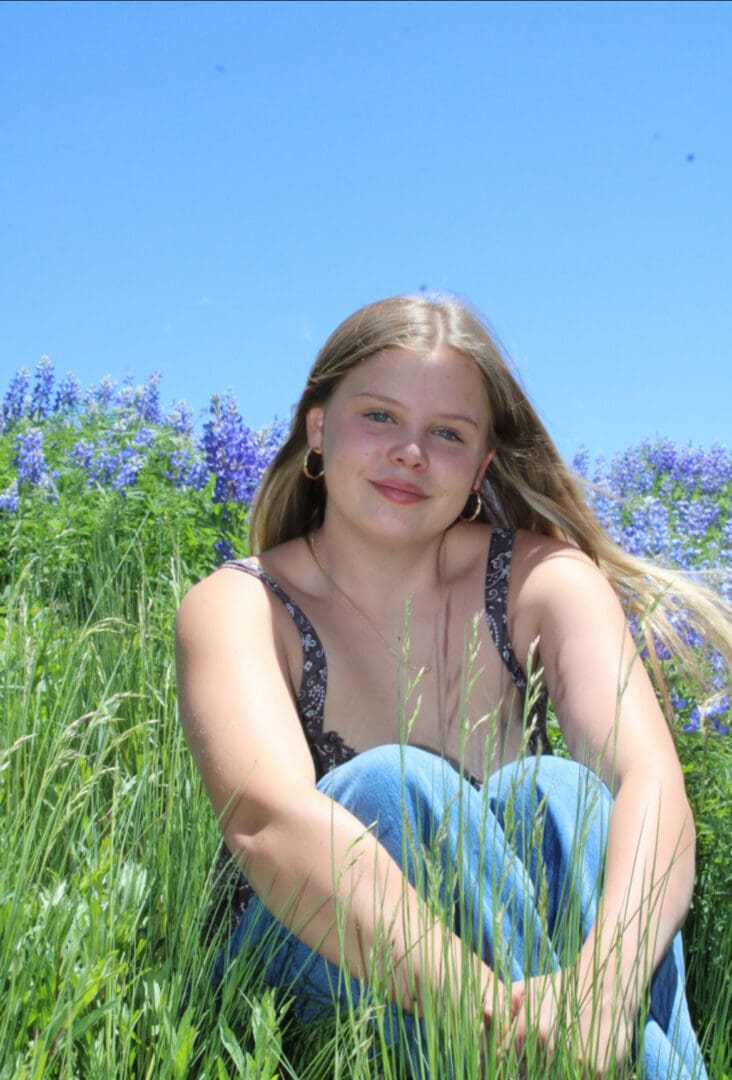 Smiling woman sitting in grassy field with flowers