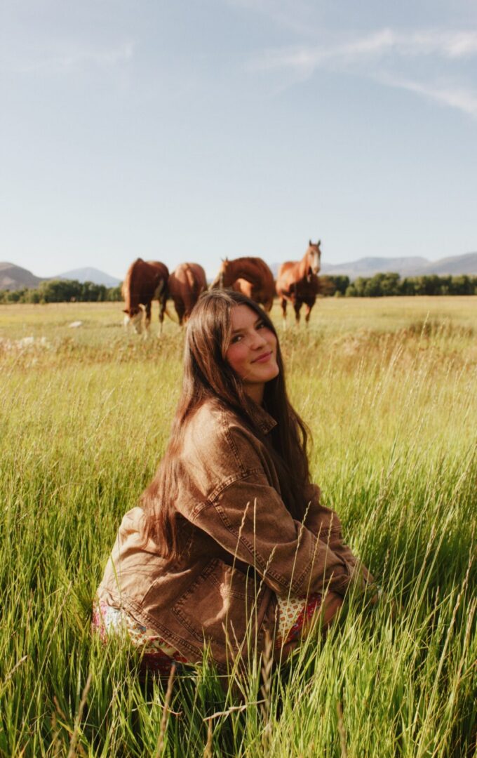Woman crouching in tall grass with horses